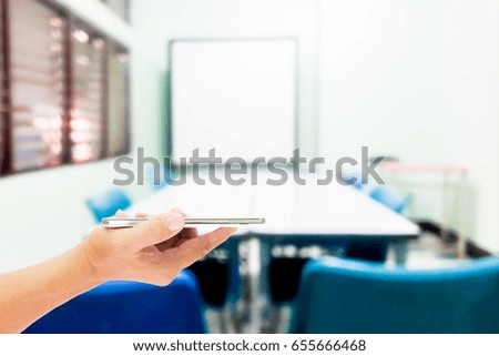 Girl use mobile phone, blur image of small and simple meeting room as background.