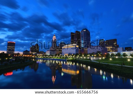 The skyline of the city of Columbus along the Scioto river at dusk with the Scioto Greenway in the foreground along the river.