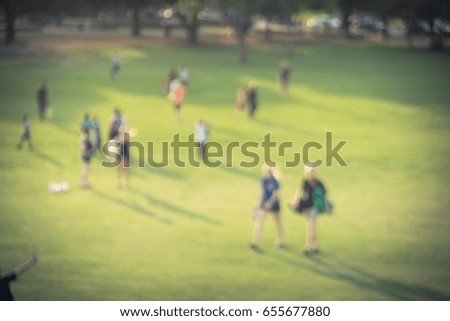 Blurred group of mixed race, ethnic, diverse culture friend and family members walking uphill in urban park at Houston, Texas, US. Down view people walk across grass hill at sunset. Vintage tone.