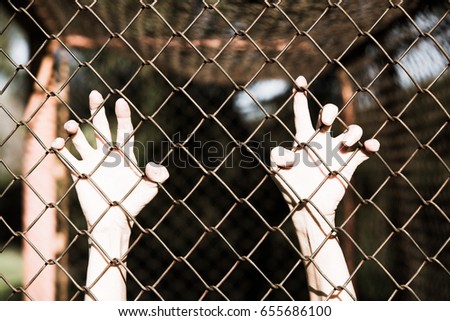 Bleached filtered image of Hands in desperate grip on mesh wired fence, symbolising captivity, hopeless, kidnapping, struggle and stressed person.