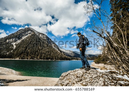 Man photographer looking for a good picture standing on a rock in mountain lake in Italy