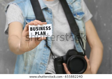 Photographer holding card with text BUSINESS PLAN and camera on color background