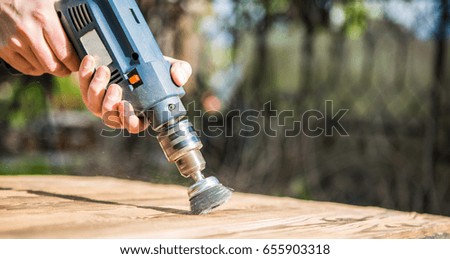 Hands man with electrical rotating brush metal disk sanding a piece of wood. Woodworking outdoors.