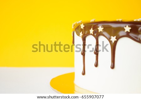 A birthday cake poured with chocolate, decorated with confectionery sprinkling stars on a yellow and white background. Close-up. Picture for a menu or a confectionery catalog.
