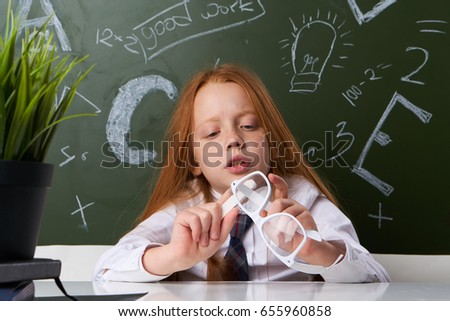 Schoolgirl is looking at glasses on the background of a blackboard                               