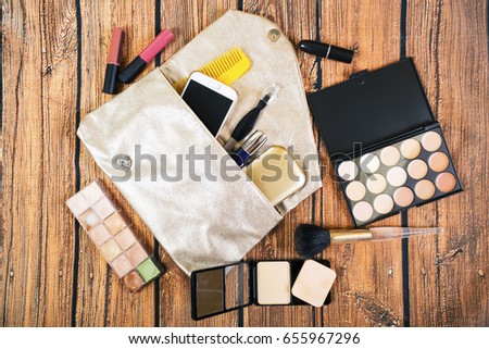 Top view accessories for woman on wooden background. Bag, powder, hairbrush, lipstick, smart phone, blush, brush, palette 