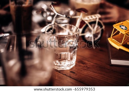 Half a glass of water at restaurant on wooden table . in concept glass full of water or a “water filled glass” . and Stay hungry, stay foolish. Tics