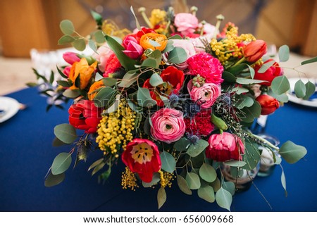 Colorful bouquet of peonies and tulips stands in the middle of blue dinner table