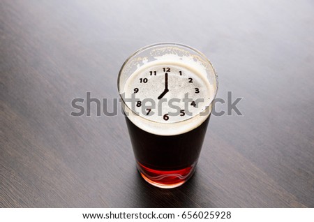 Clock silhouette on foam in beer glass on black table, view from above.