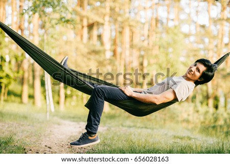Happy peruvian young man resting and relaxing in hammock outdoor on nature in forest in summer sunny day with pine trees and green grass. Travel, holidays, tourism, vacation. Dreaming in park.