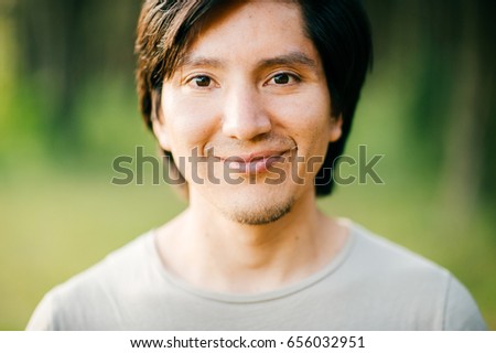 Close up  portrait of native american peruvian indian man with black hair, dark eyes looking at camera with deep reflective and stare eyes. Nature, park, outdoor. Abstract background. 