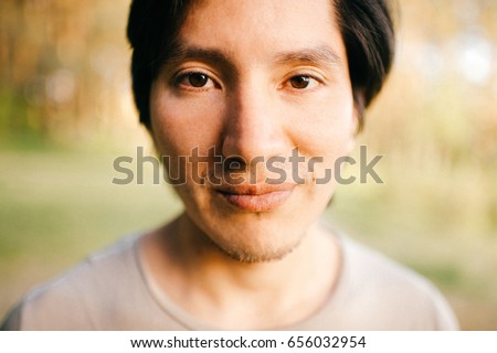 Close up  portrait of native american peruvian indian man with black hair, dark eyes looking at camera with deep reflective and stare eyes. Nature, park, outdoor. Abstract background. 