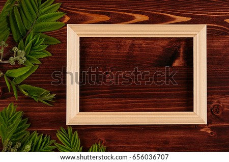 Blank photo wood frame and young green leaves on vintage brown wooden board. Decorative summer background with copy space, top view.