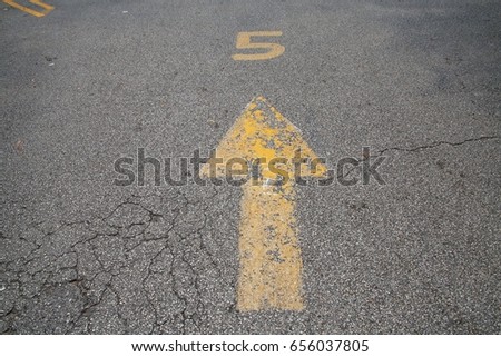 Yellow Arrow with Number 5 Above Painted on Parking Lot Pavement