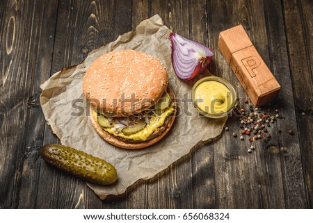 Tasty hamburger with onion and pickled cucumbers on wooden table.