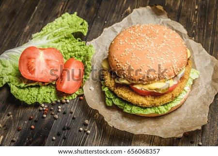 From above appetizing hamburger with tomato and green salad leaf on wooden table.