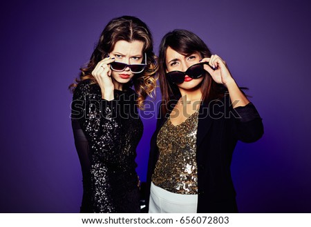 Attractive young women lowering sunglasses and making faces while having photo shoot in studio, waist-up group portrait