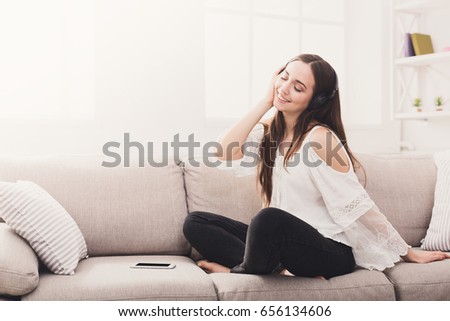 Happy girl in headphones listening to music. Relaxed woman on the couch with closed eyes, mobile lying near, copy space