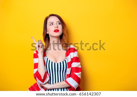 Beautiful Portrait of young surprised red-haired white european woman in red striped shirt with on yellow background