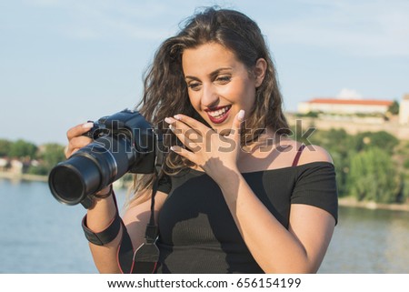 Woman tourist on the street. Under sunlight and blue sky. Female photographer with a professional camera. Portrait of a beautiful laughing brunette girl, making photos by the river.
