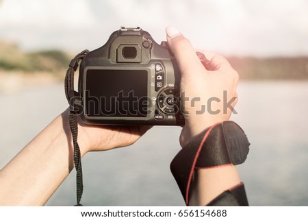 Close-up of female hands holding a professional camera. Female photographer with a professional camera. Lens flare in the background.