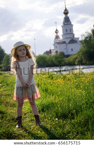 Portrait of a cute little girl in a hat on a summer day against the backdrop of a church in the village