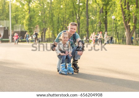 Little girl and her father posing and roller skating in protective form together on weekend
