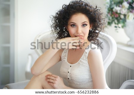 Emotional portrait of a cute curly girl covering her mouth with a palm.