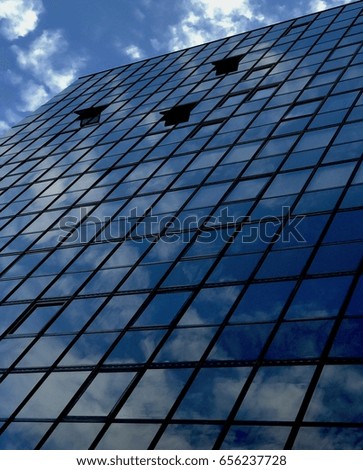 Facade of a modern steel and glass building with the sky and clouds reflected on it