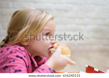 Adorable girl eat classic burger in fast food restaurant