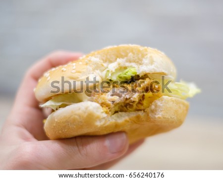 Bitten classic burger in hand in fast food restaurant