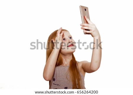 Red-haired girl with phone. A child makes selfie on a smartphone