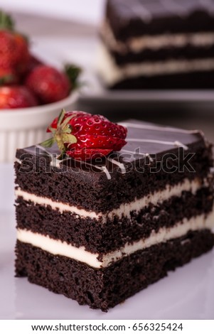 Slice of chocolate tuxedo cake with strawberries and cake in the background