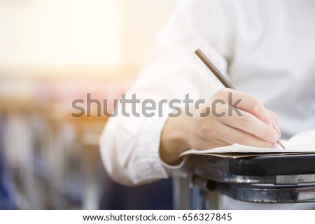 soft focus front view undergraduate holding pencil writing on paper answer sheet and sitting on lecture chair doing final exam attending in examination room or classroom.university student in uniform. Royalty-Free Stock Photo #656327845