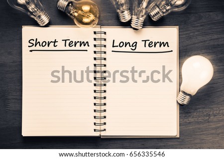 Short term and Long term on opened notebook with glowing light bulb Royalty-Free Stock Photo #656335546