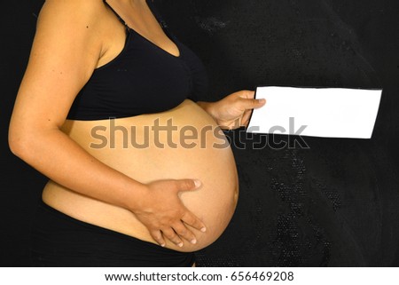 A pregnant woman holding up a note with room for text.