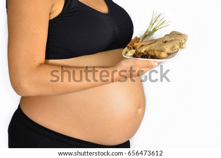 A pregnant woman graciously holding up a plate of spices like ginger roots and cinnamon sticks.