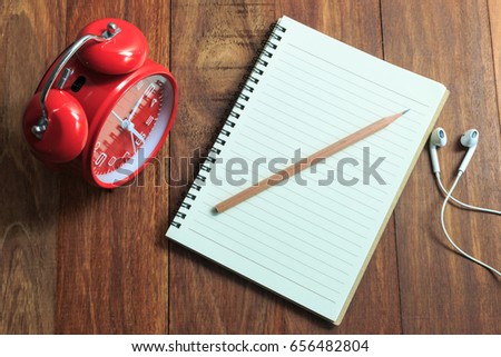 Red clock on wooden with notepad and pencil
