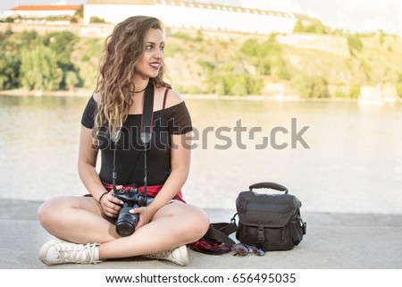 Portrait of a beautiful female photographer with a professional camera. Woman photographer with a professional camera and bag. Beautiful day by the river. Lens flare in the background.