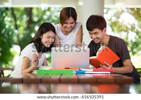 Three asia teenage students smiling at a laptop on a wooden desk, Background is bokeh from a tree and light, Young gerneration and Education concept.