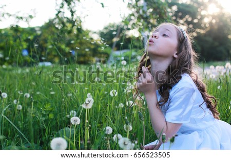 A teen blowing seeds from a dandelion flower in a spring park