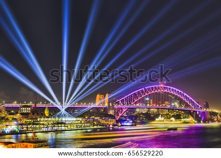 Colourful illumination of Sydney Harbour bridge and overseas passenger terminal around Circular Quay and The Rocks during Vivid Sydney light show and festival. Royalty-Free Stock Photo #656529220