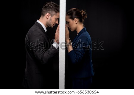 Side view of sad couple in formal wear separated by wall isolated on black Royalty-Free Stock Photo #656530654