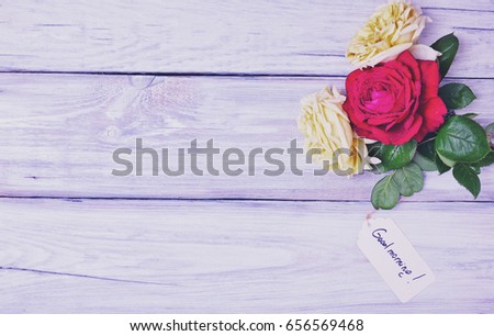 Three blossoming roses on a white wooden background with a paper tag and an inscription good morning, vintage toning
