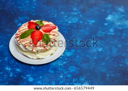 White creamy round cake with strawberries and mint on plate, blue background, copyspace.