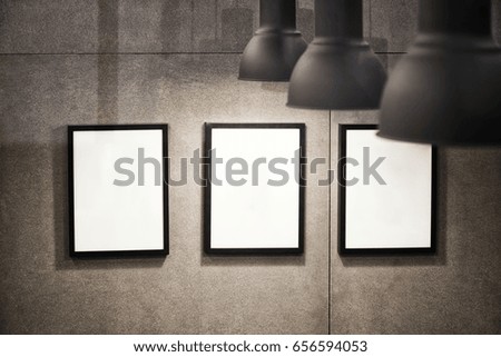 Three white picture frames with black border hanged on loft concrete wall with black industrial style lamps.