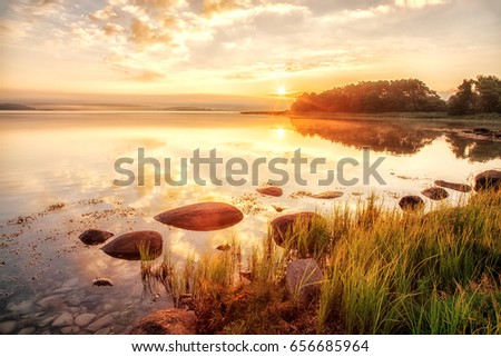 Sunrise scenery over Northern sea in Sweden, coast line with green grass an foreground, epic sunrise sky in background.