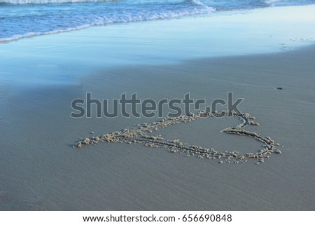 Heart hand drawn in sand on isolated deserted beach by ocean shore at sunset on a calm and peaceful beautiful evening; romantic wedding night, Valentine's day, and love concept with sandy copy space
