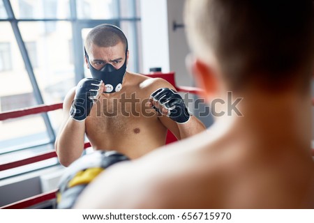 Portrait of young boxer wearing endurance training mask fighting with opponent in boxing ring