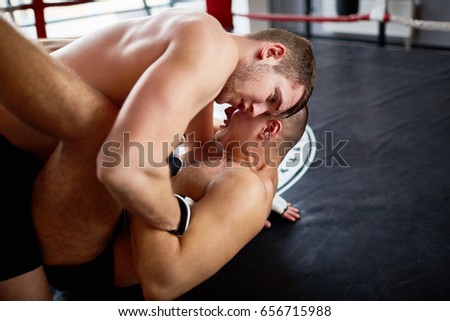 Portrait of shirtless wrestlers fighting in boxing ring: tackling opponent to floor and performing submission hold